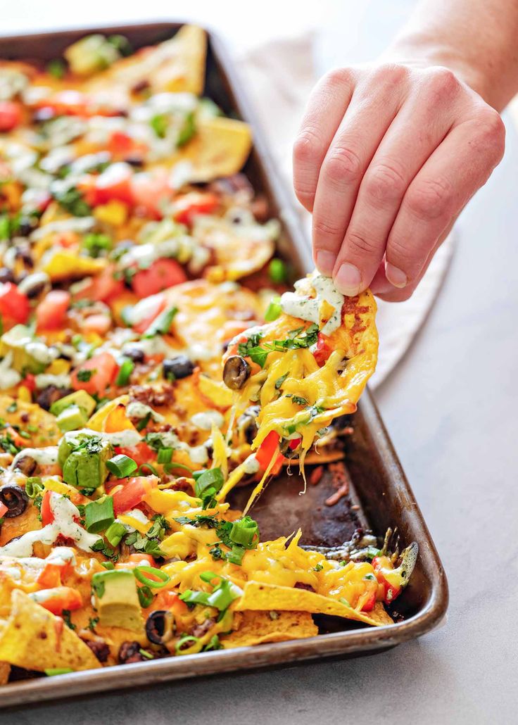 a person dipping tortilla chips into a baking pan filled with nachos