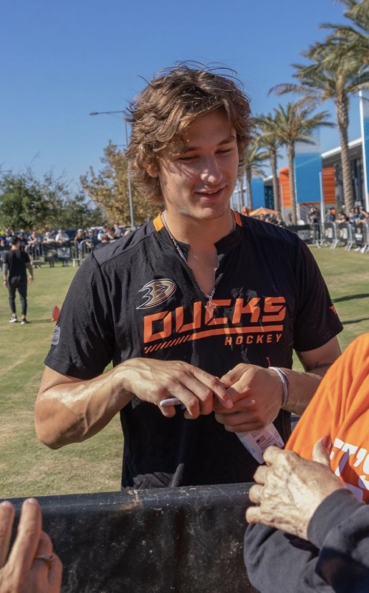 a man in an orange and black shirt is handing something to another person on his cell phone