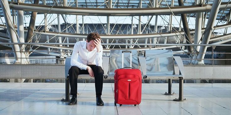 a man sitting on a bench next to a red piece of luggage in an airport