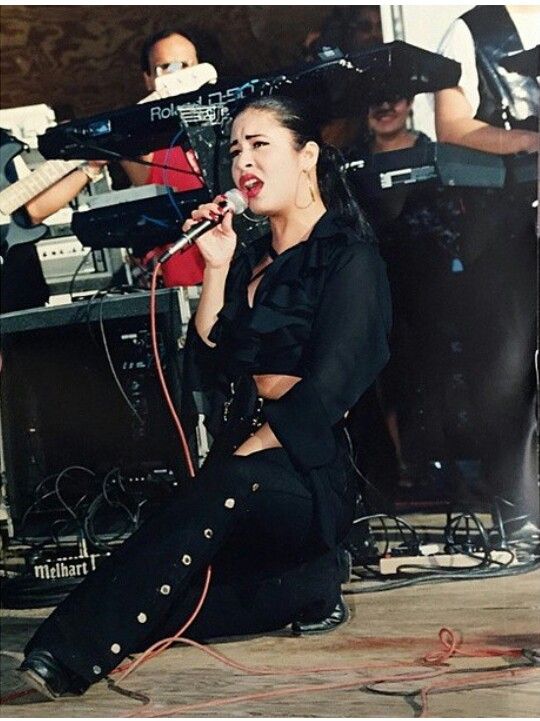 a woman sitting on the ground while holding a microphone in her hand and singing into a mic