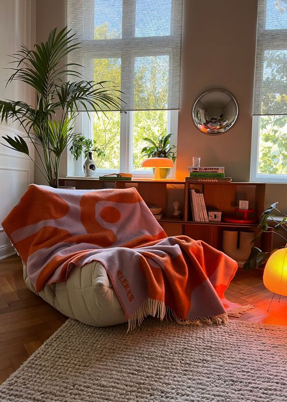 an orange and white blanket sitting on top of a bean bag chair next to a window