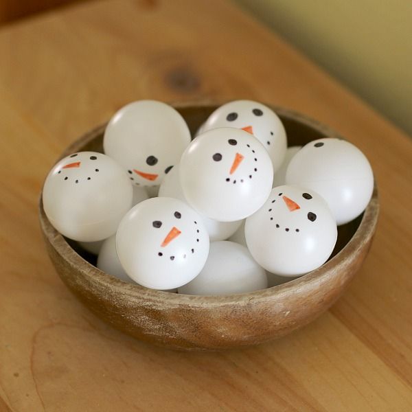 a bowl filled with white plastic snowmen sitting on top of a wooden table