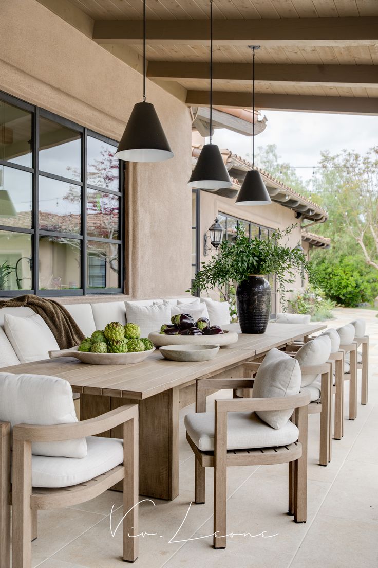 an outdoor dining area with white cushions and wooden tables, hanging lights and potted plants