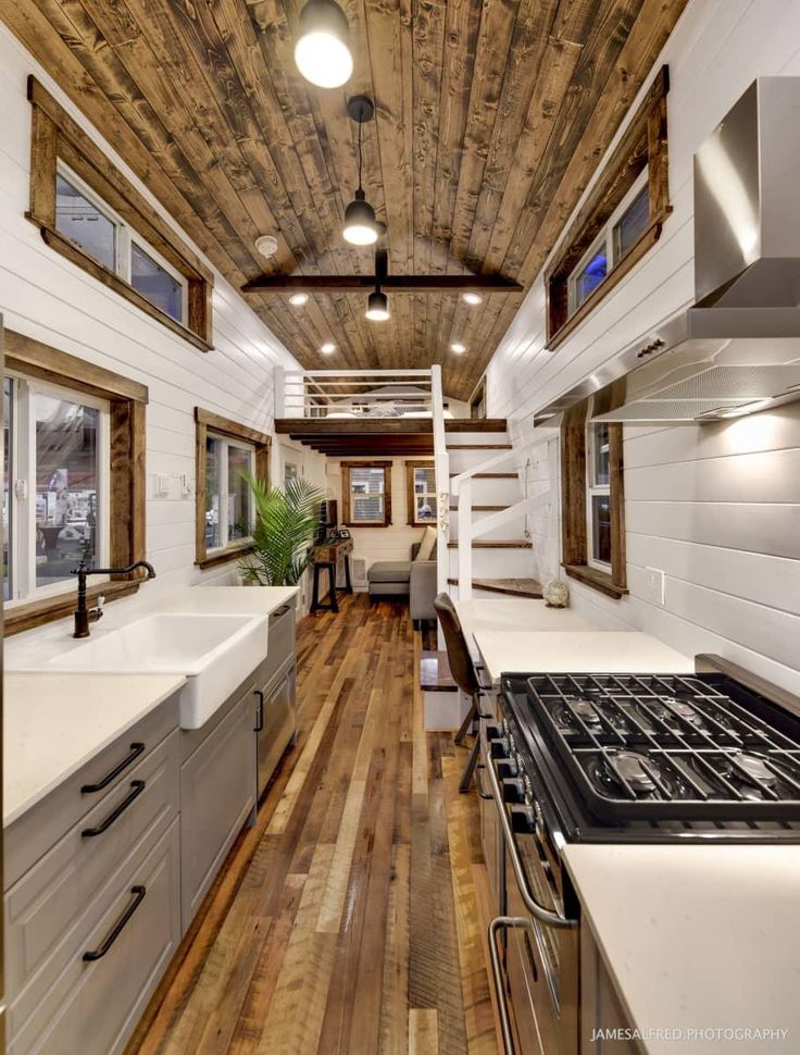 the interior of a tiny house with wood flooring and white counter tops, along with stainless steel appliances