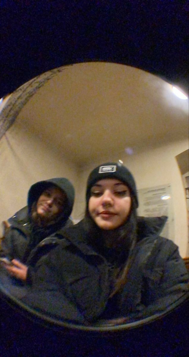 two people are taking a selfie in a mirror with one person wearing a beanie and the other holding a cell phone