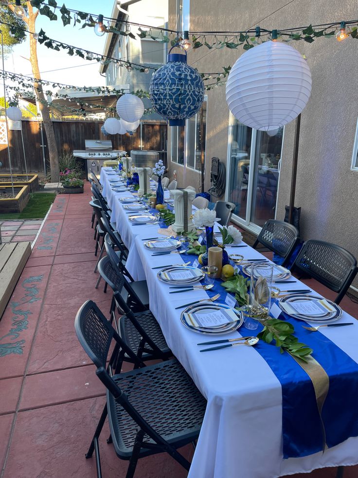 a long table set up with plates and silverware for an outdoor dinner or party