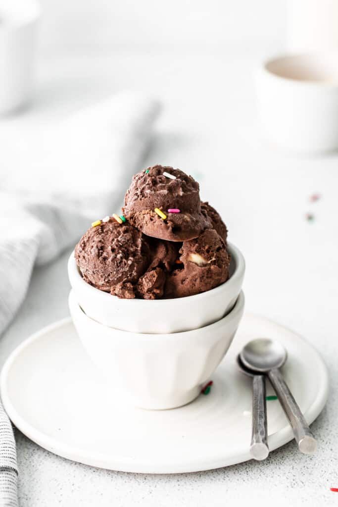 three scoops of chocolate ice cream in a white bowl with sprinkles