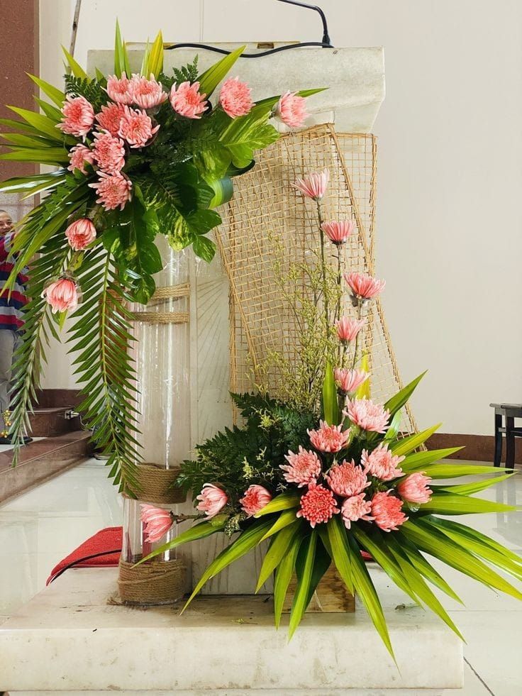 pink flowers and greenery on display in front of a white vase with green leaves