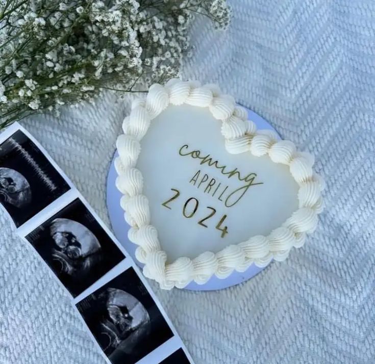 a heart shaped cake sitting on top of a table next to some flowers and photos