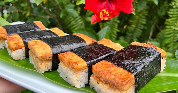 sushi is served on a green leafy plate with flowers in the back ground