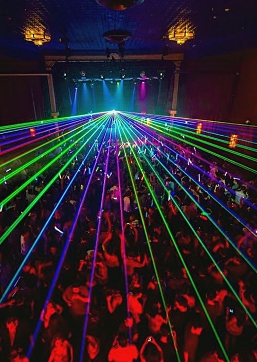 a large room filled with lots of people and laser lights on the ceiling, all in different colors