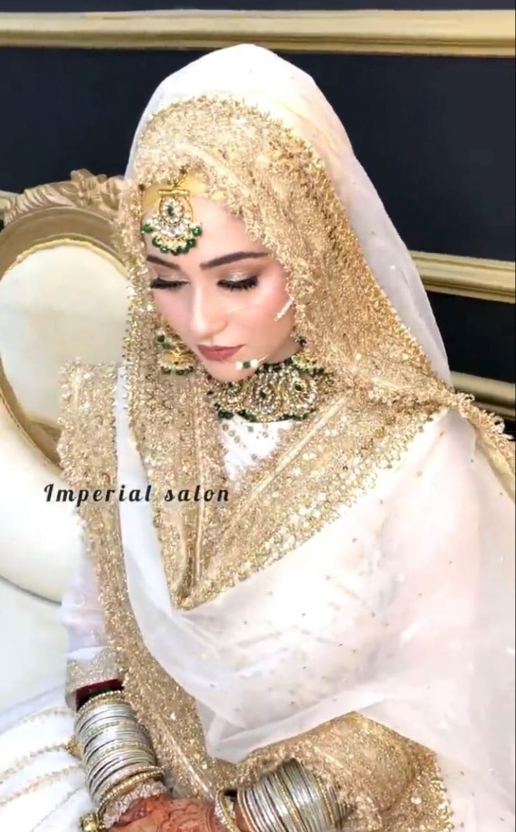 a woman in a white and gold wedding outfit sitting on a couch with her hands together