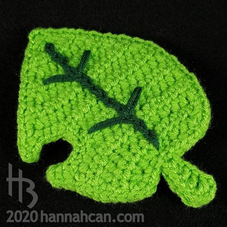 a crocheted green hat with a leaf on it's side, sitting on a black surface