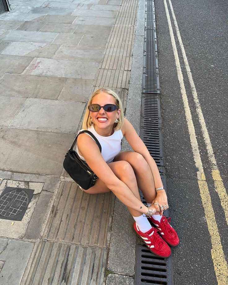 a woman is sitting on the curb with her red shoes