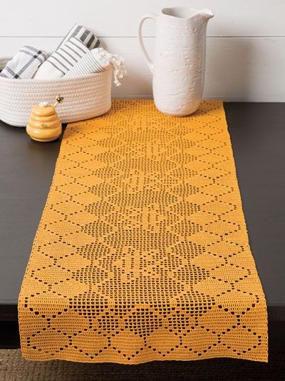 a yellow table runner sitting on top of a wooden table next to a white vase