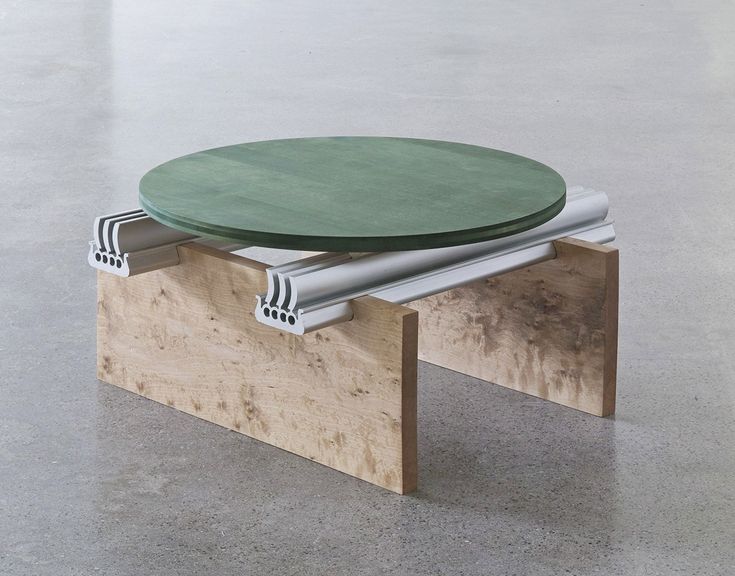 a green table sitting on top of a wooden bench next to a white wall and floor