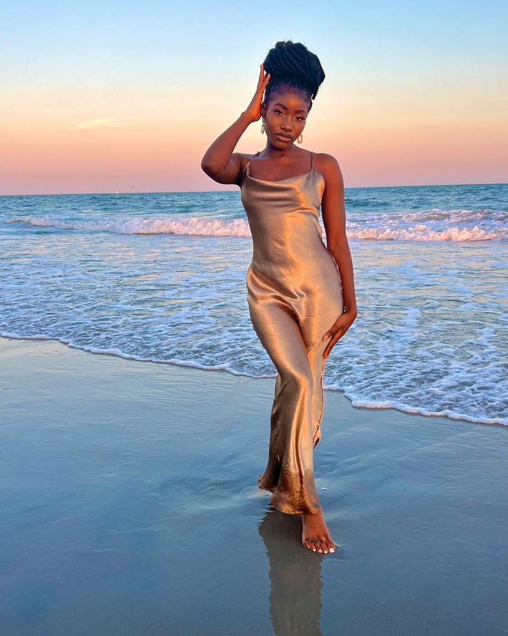 a woman standing on top of a sandy beach next to the ocean with her hand in her hair