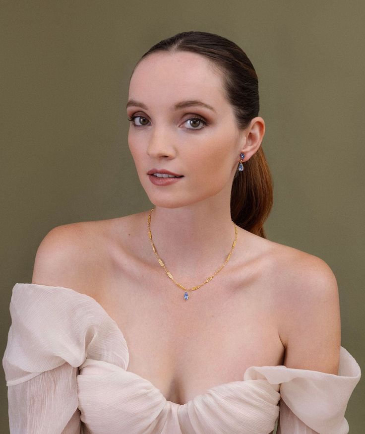 a woman in a white dress with large breast wearing a gold necklace and diamond earrings