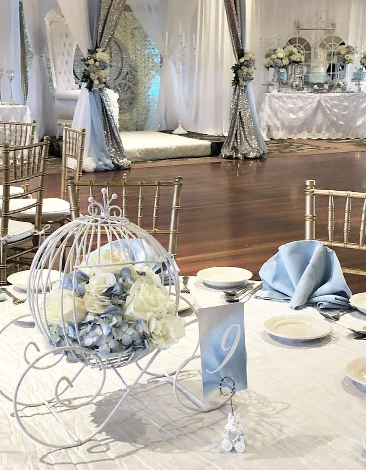 a table set up for a wedding with white and blue flowers in a birdcage