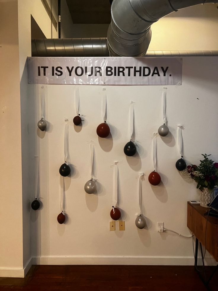 there is a sign that says it is your birthday hanging on the wall next to some balls