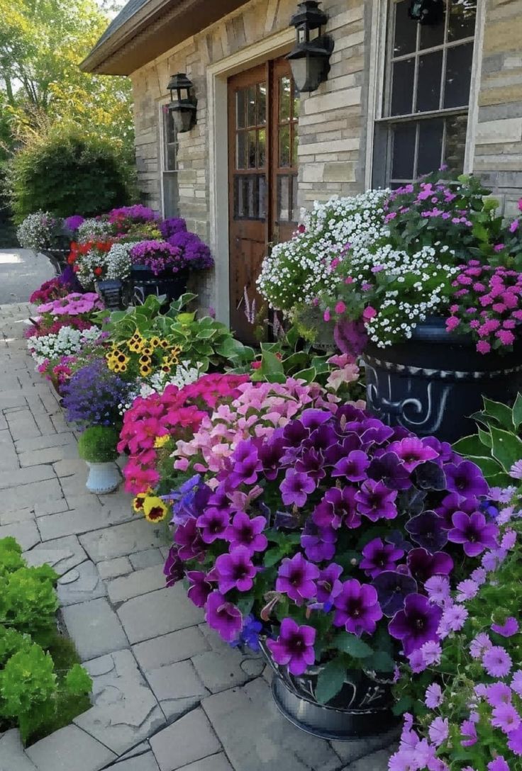 colorful flowers line the side of a building in front of a brick walkway and door