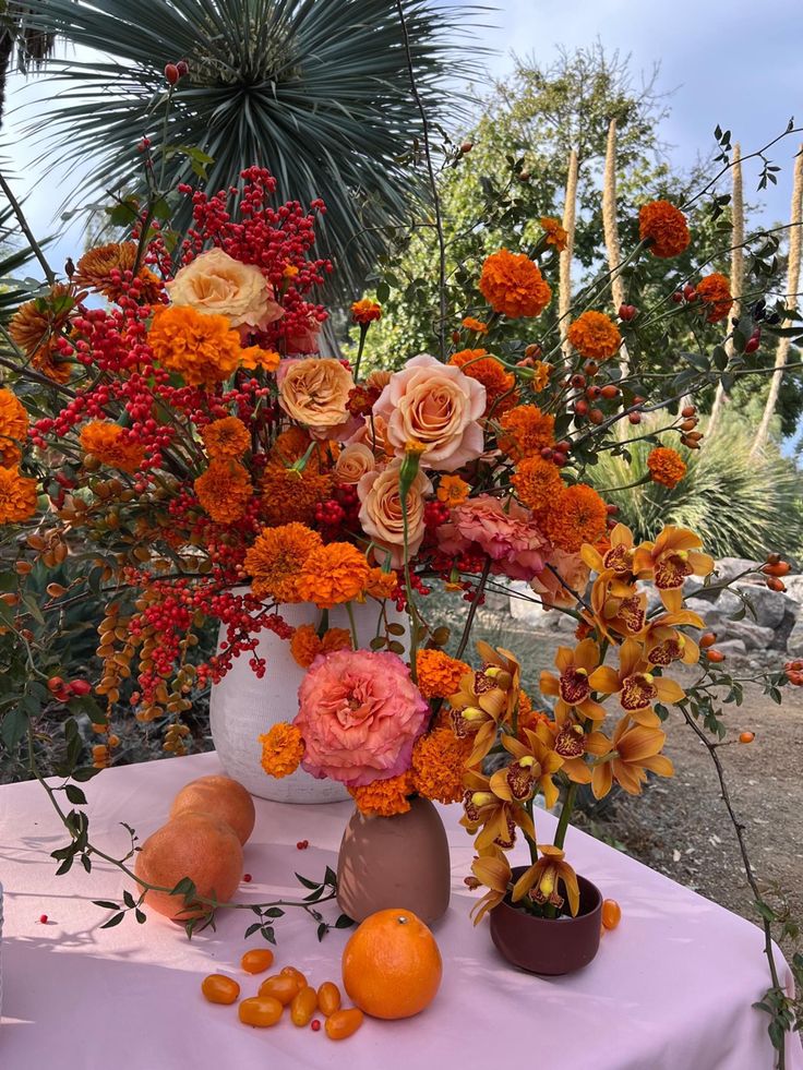 an arrangement of flowers and oranges on a table in front of some palm trees