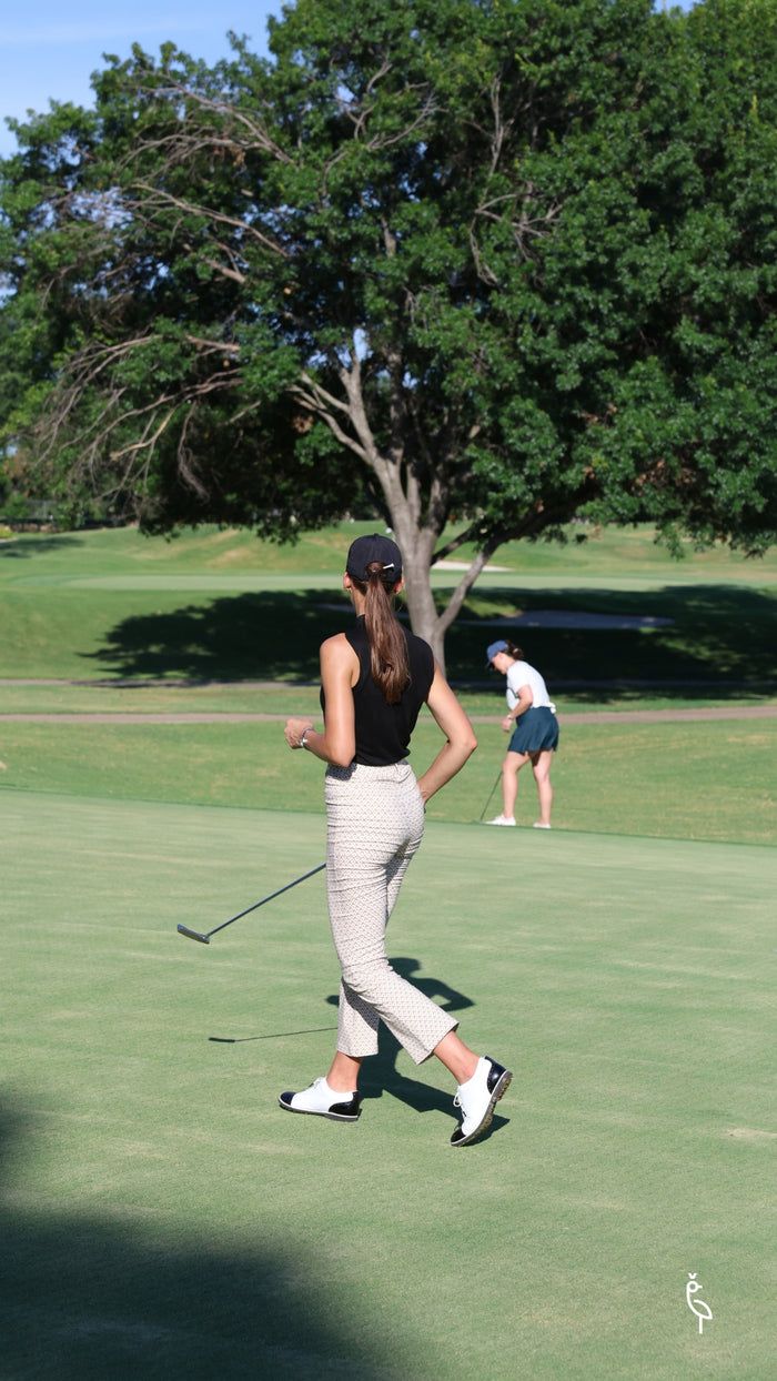 a woman walking across a green field holding a golf club