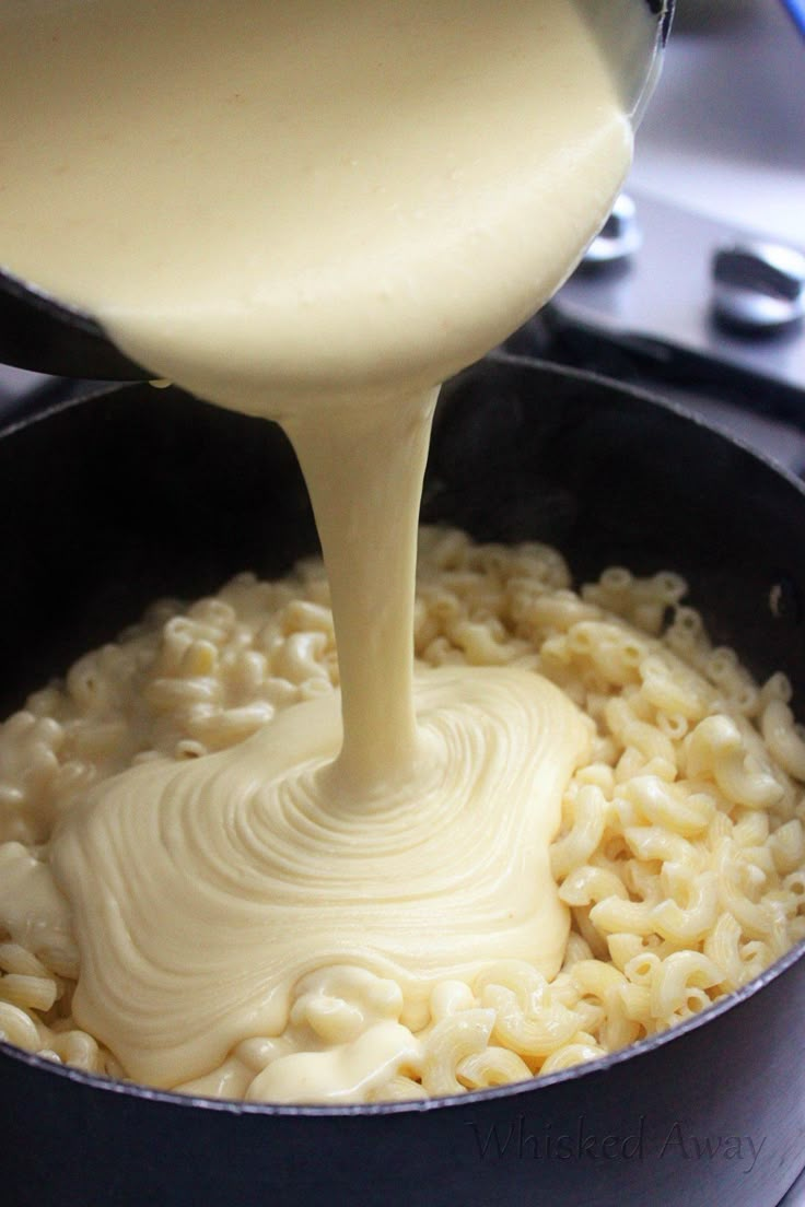 a pan filled with macaroni and cheese being poured over it's top