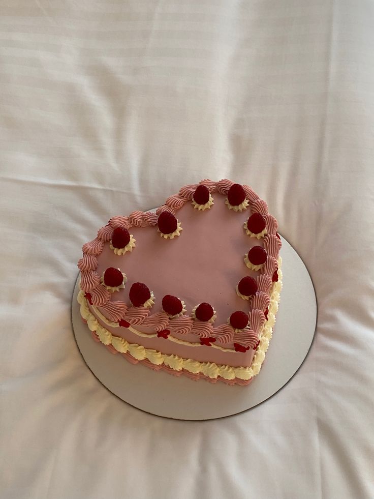 a heart shaped cake sitting on top of a white tablecloth covered bed with pillows