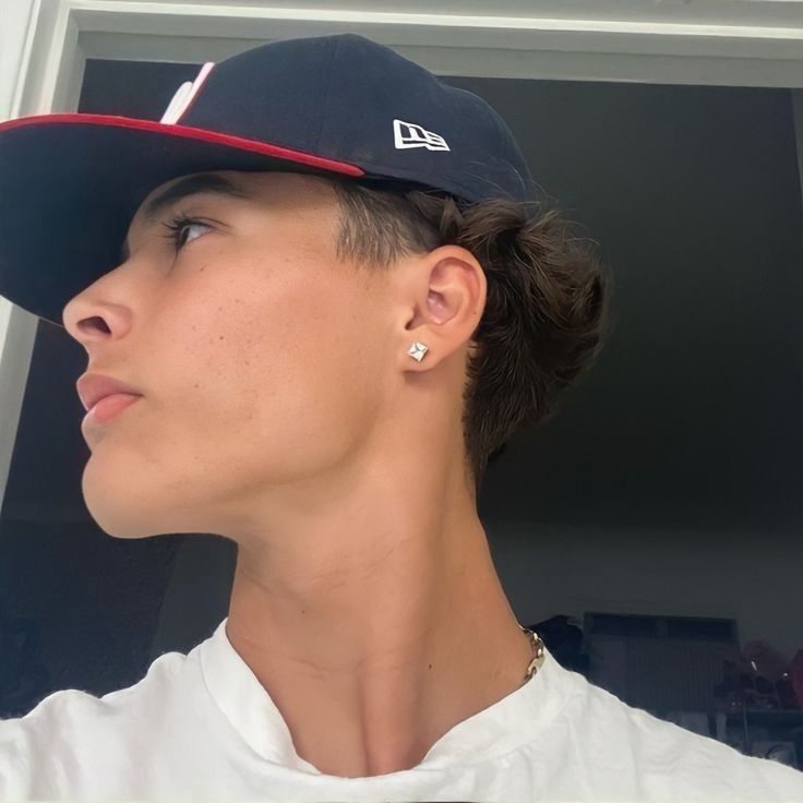 a young man wearing a new era baseball cap and earring is looking off into the distance