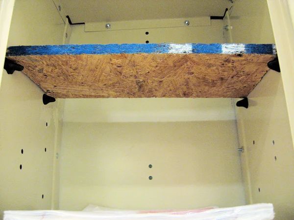 an unfinished wooden shelf with blue tape on the bottom and black brackets hanging from it's sides