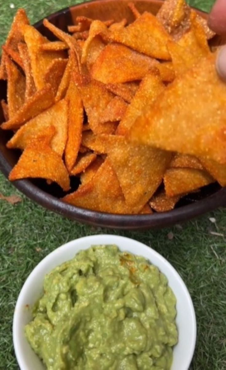 someone is dipping guacamole in a bowl with chips on the ground next to it