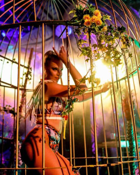 a woman is standing in a cage with flowers on her head and holding onto the bars