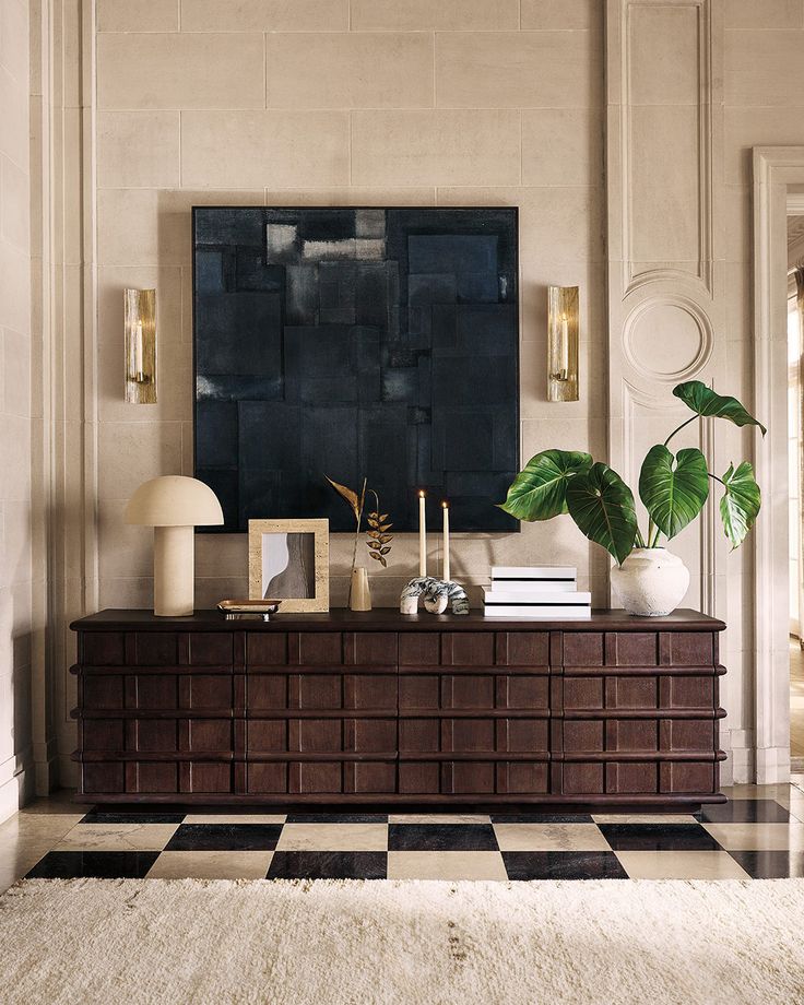 a living room with a large painting on the wall next to a dresser and lamp