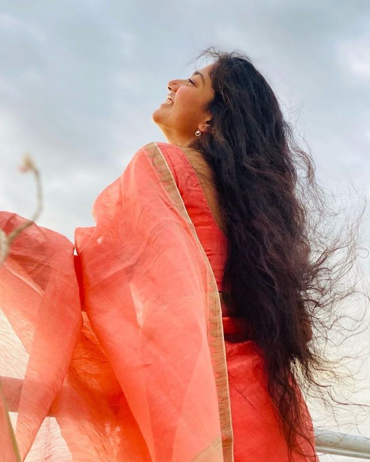 a woman with long black hair wearing an orange sari and looking up into the sky