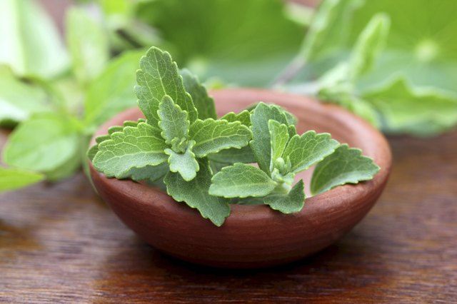 a wooden bowl filled with green leaves on top of a table