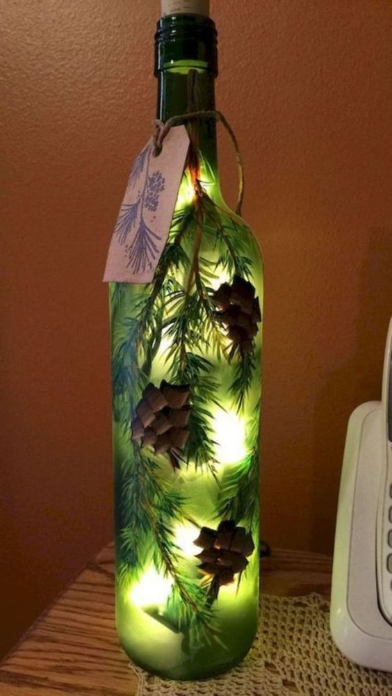 a lighted bottle with pine cones on it sitting next to a phone and remote control