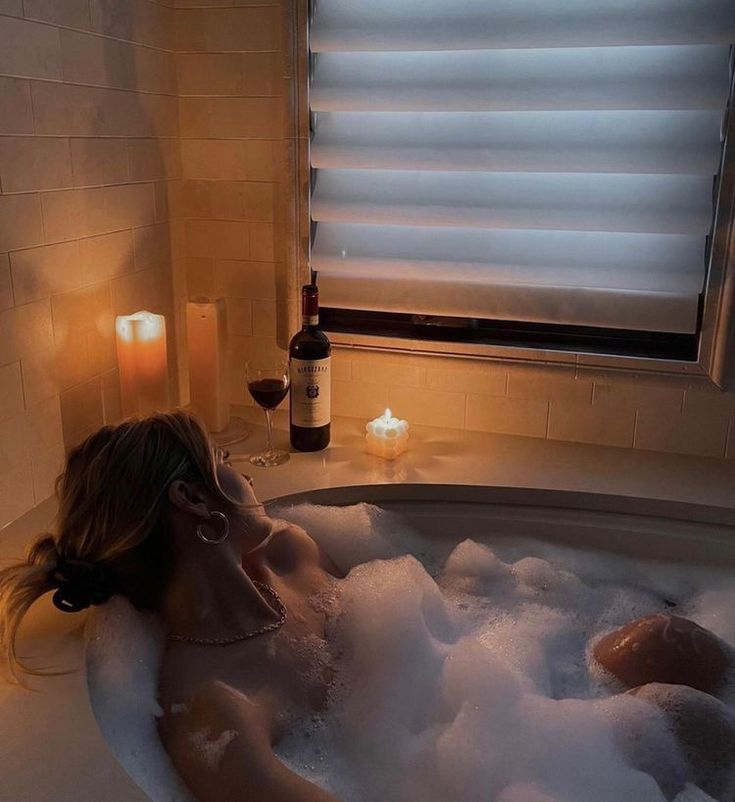 a woman laying in a bathtub with foamy bubbles and candles around her feet