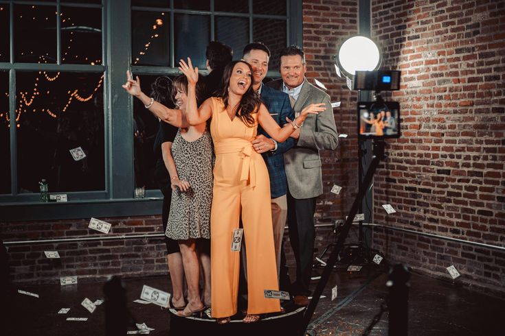 three people standing in front of a brick wall with papers flying around them and one person taking a selfie