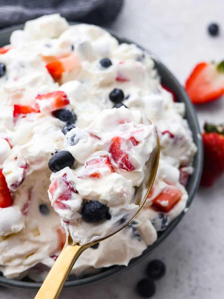 a bowl full of fruit salad with a spoon in it and strawberries on the side