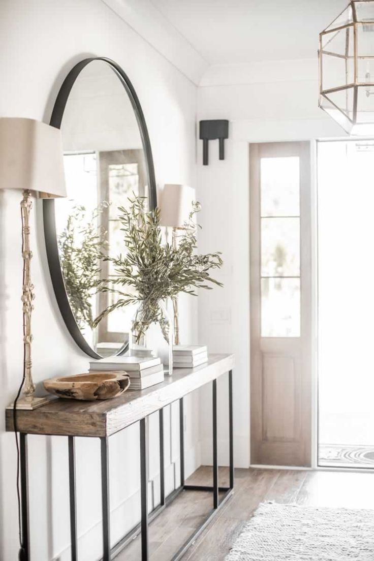 a mirror on the wall above a console with a plant in it and a lamp next to it