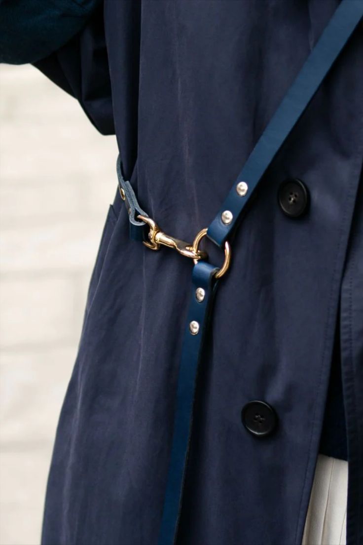 a woman wearing a blue trench coat with a gold chain on the belt and white pants