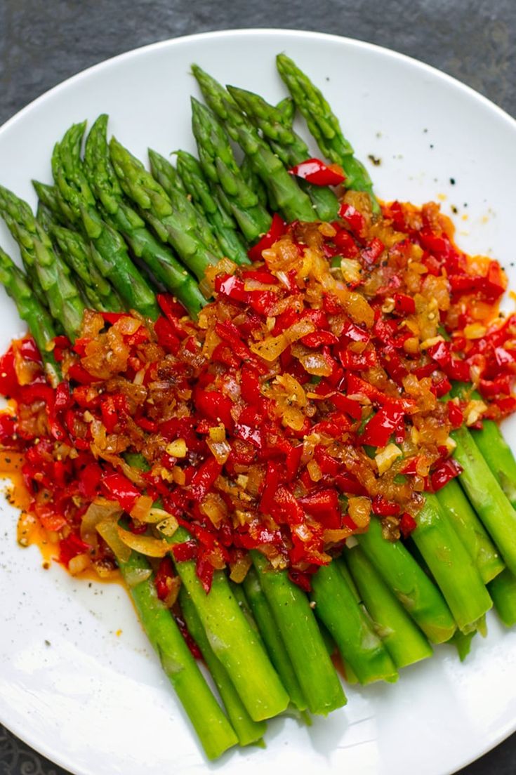 asparagus with red sauce and onions on a white plate, ready to be eaten