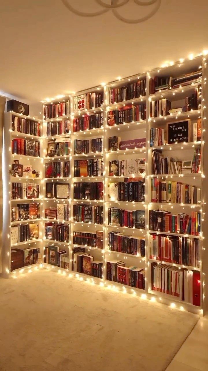 a room filled with lots of books and lights on the wall next to a window