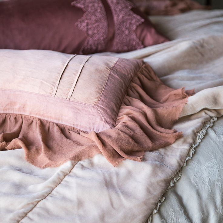 pillows and blankets on a bed in a bedroom with white sheets, pink linens