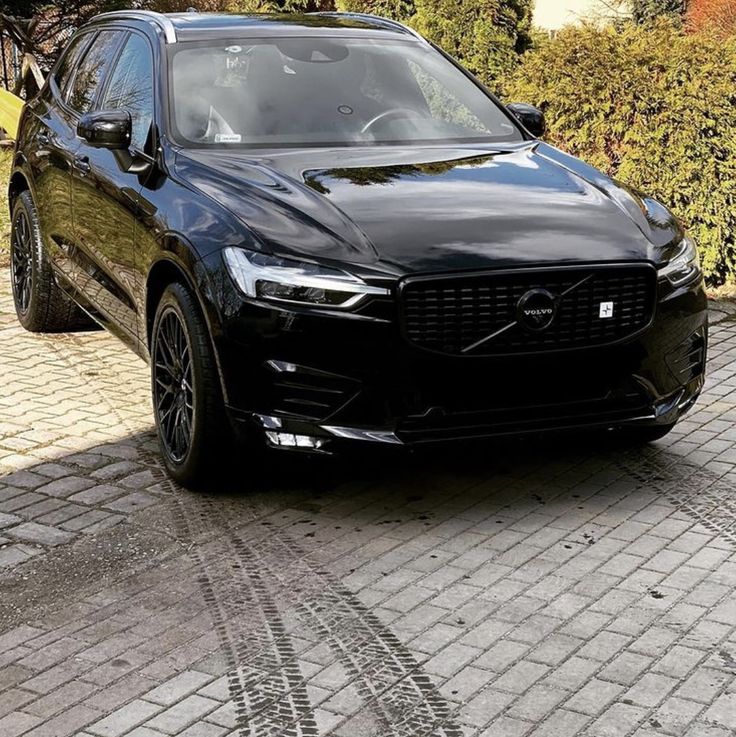 a black volvo car parked in front of a house on a cobblestone driveway