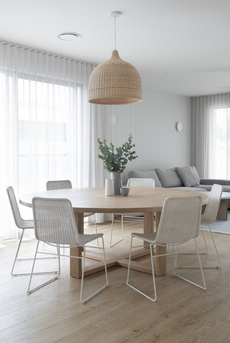 a dining room table with four chairs and a couch in the background, along with a large window