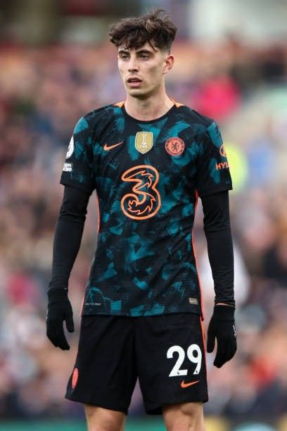 a soccer player standing on the field with his hands in his pockets and wearing black gloves