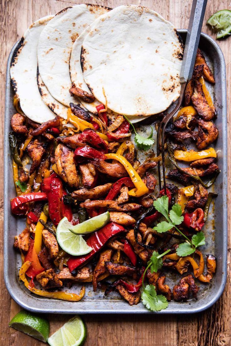 chicken fajitas and tortillas on a tray with limes, cilantro, and peppers