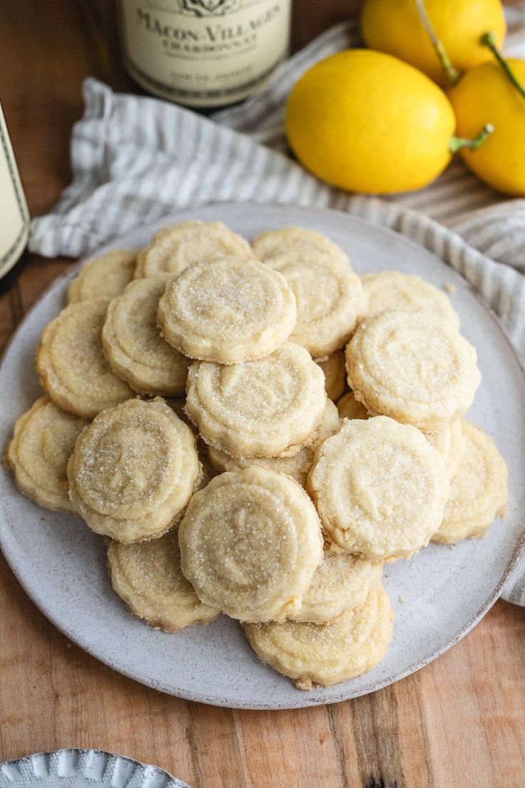 a plate full of lemon cookies next to two bottles of wine and some lemons